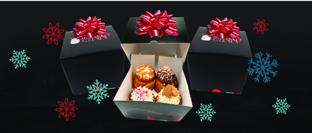 WannaCinn Holiday Box - shows three boxes with colorful snowflakes falling around it. One box is open, showcasing four specialty Cinns. 